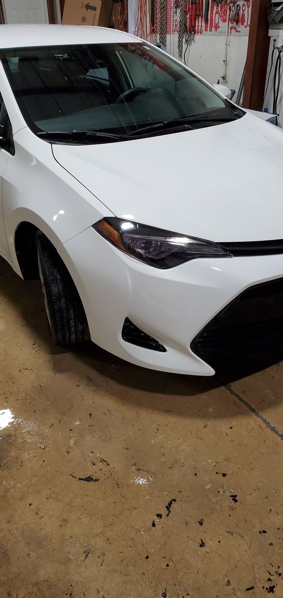 White Toyota Corolla car in a garage with a wet concrete floor.