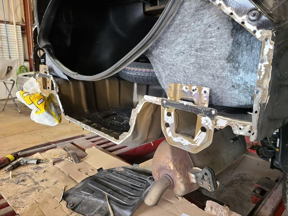 Car trunk area with damaged body panels being repaired. Exposed metal frame, spare tire visible.
