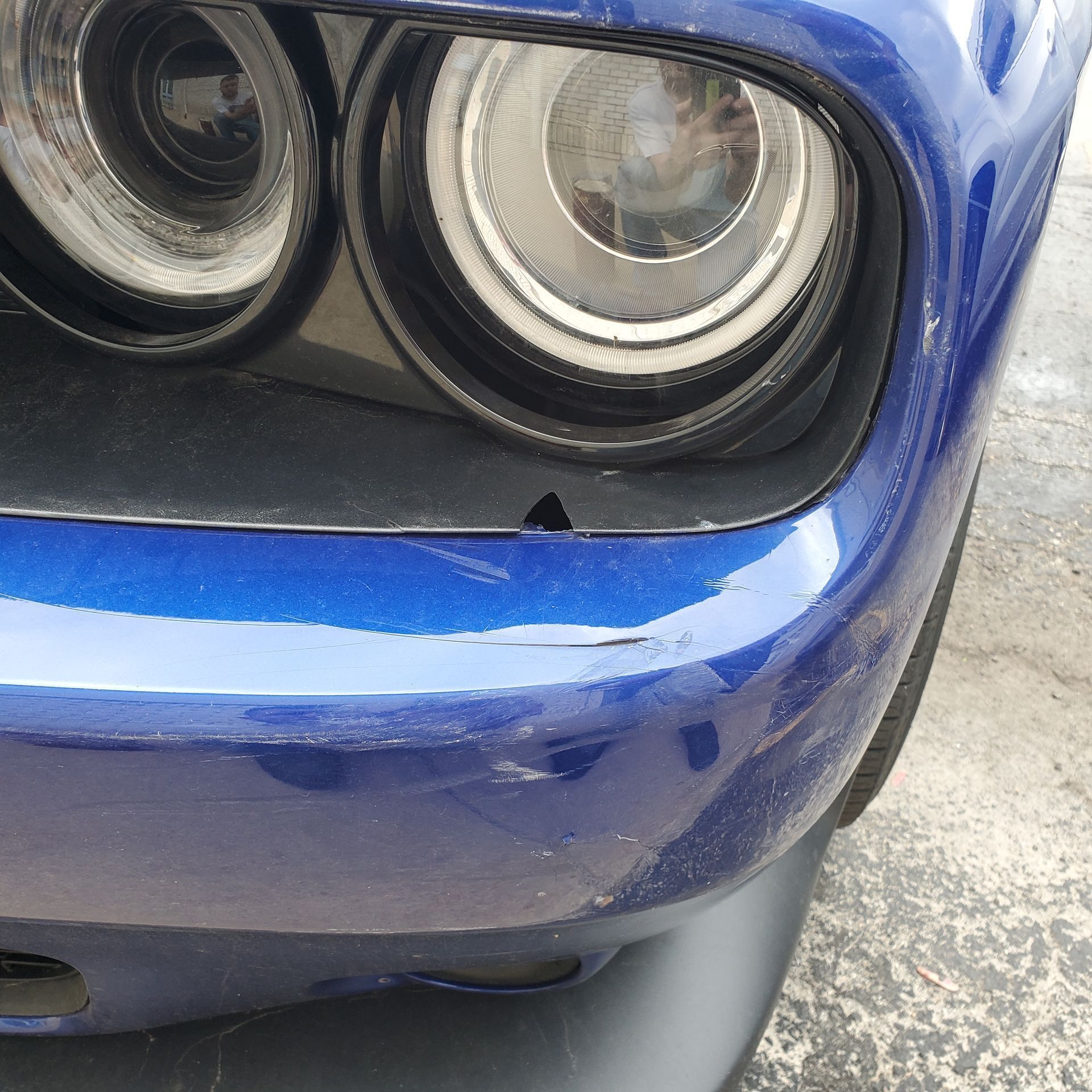 Blue car's headlight close-up, small triangle-shaped paint chip visible on the bumper below the headlight.