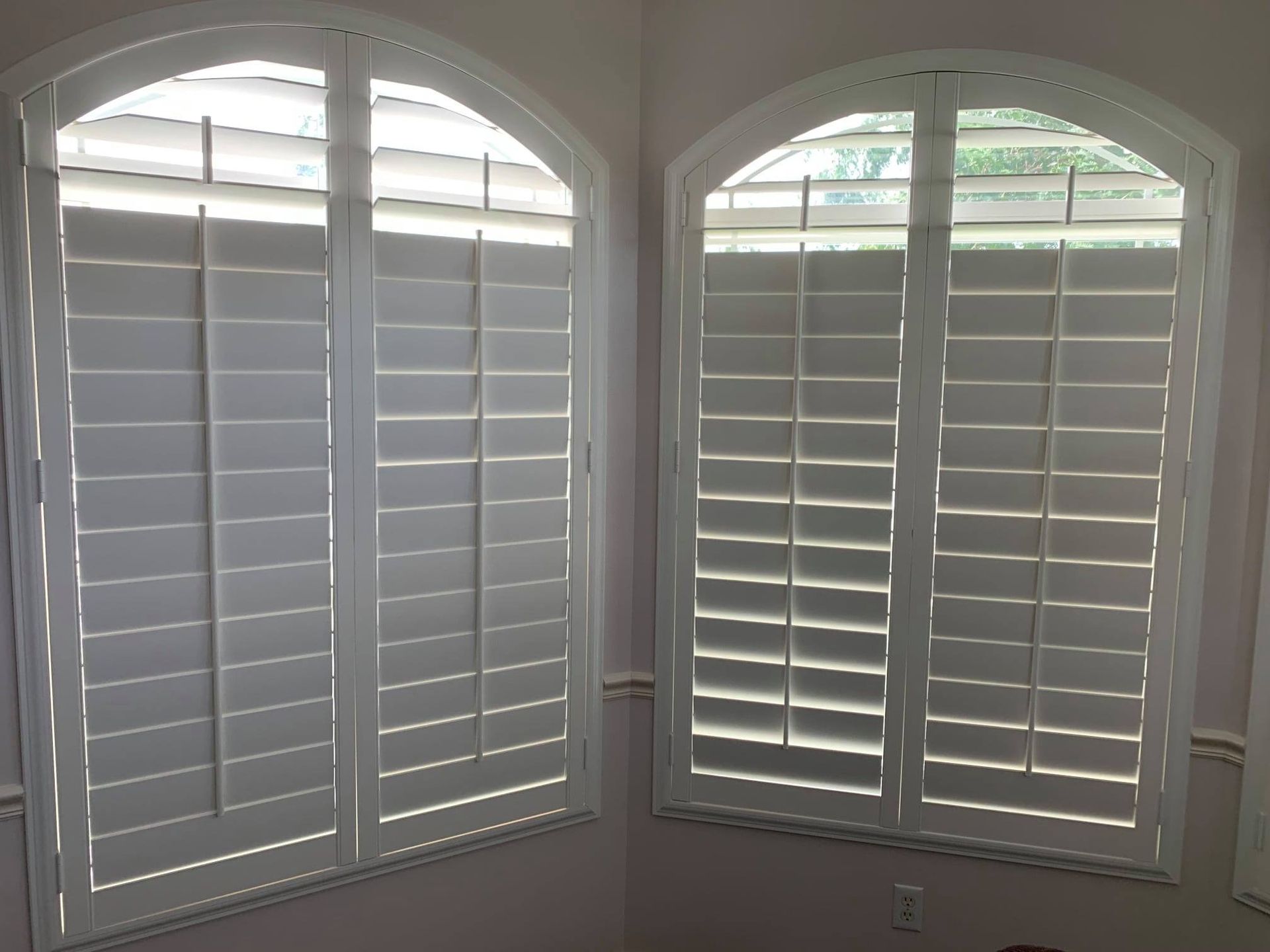 Two arched windows with white shutters in a room