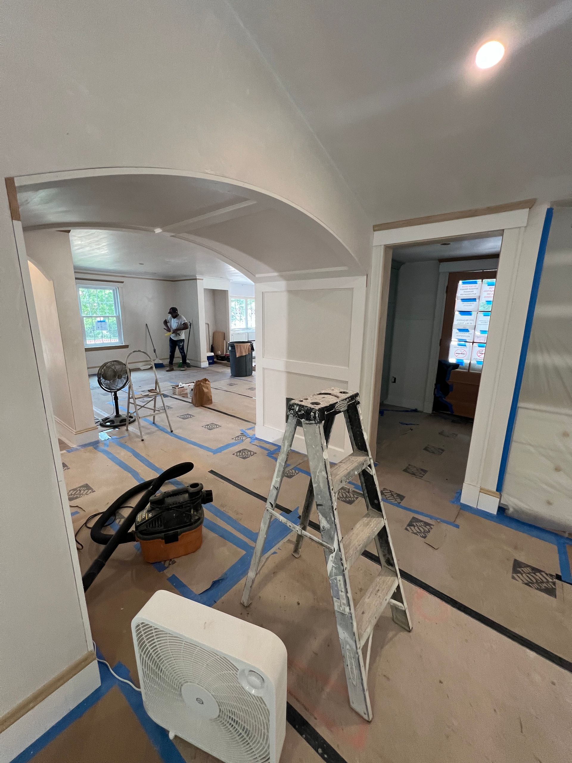 A room is being painted with a ladder , fan , and vacuum cleaner.