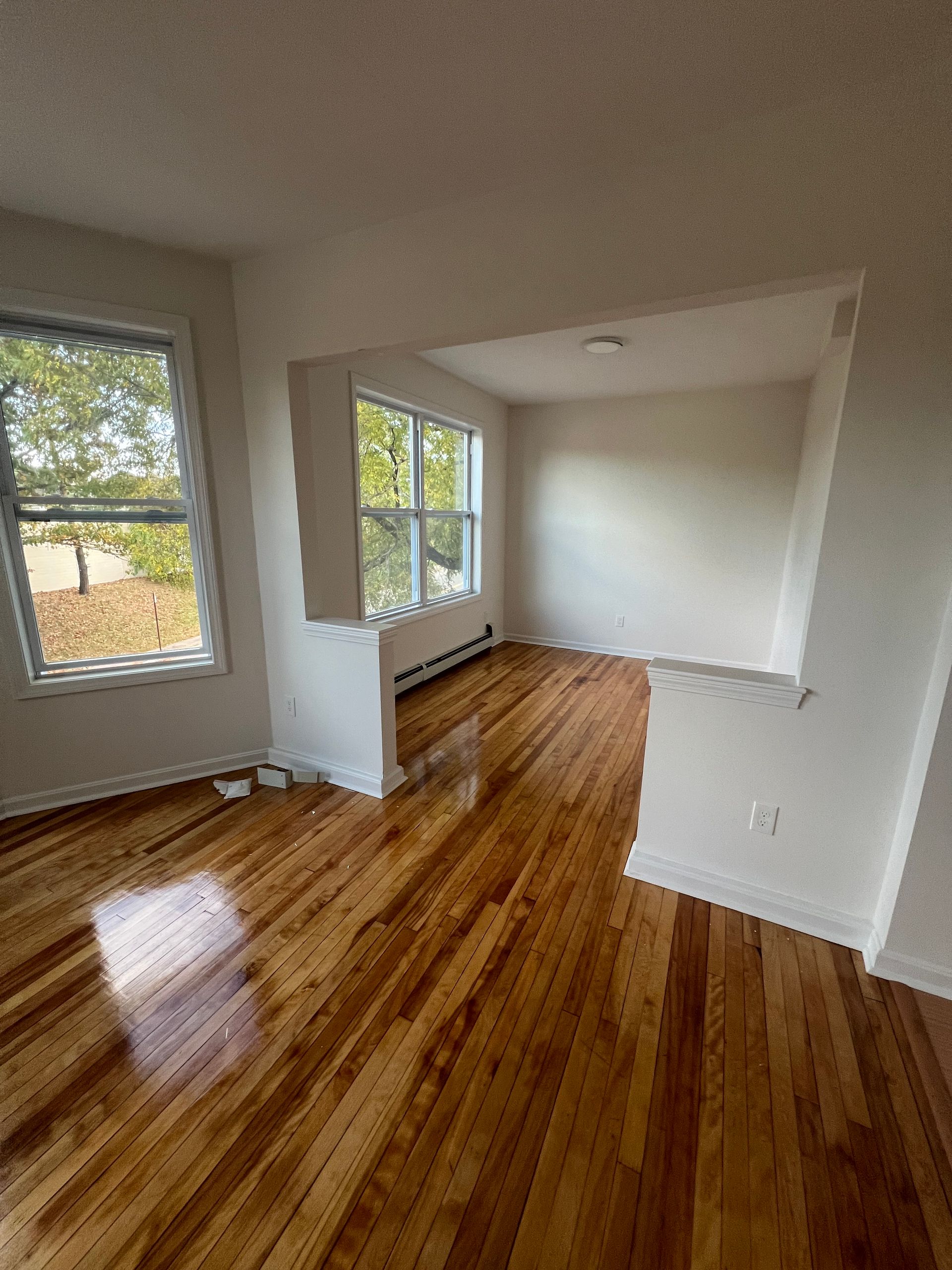An empty living room with hardwood floors and white walls.