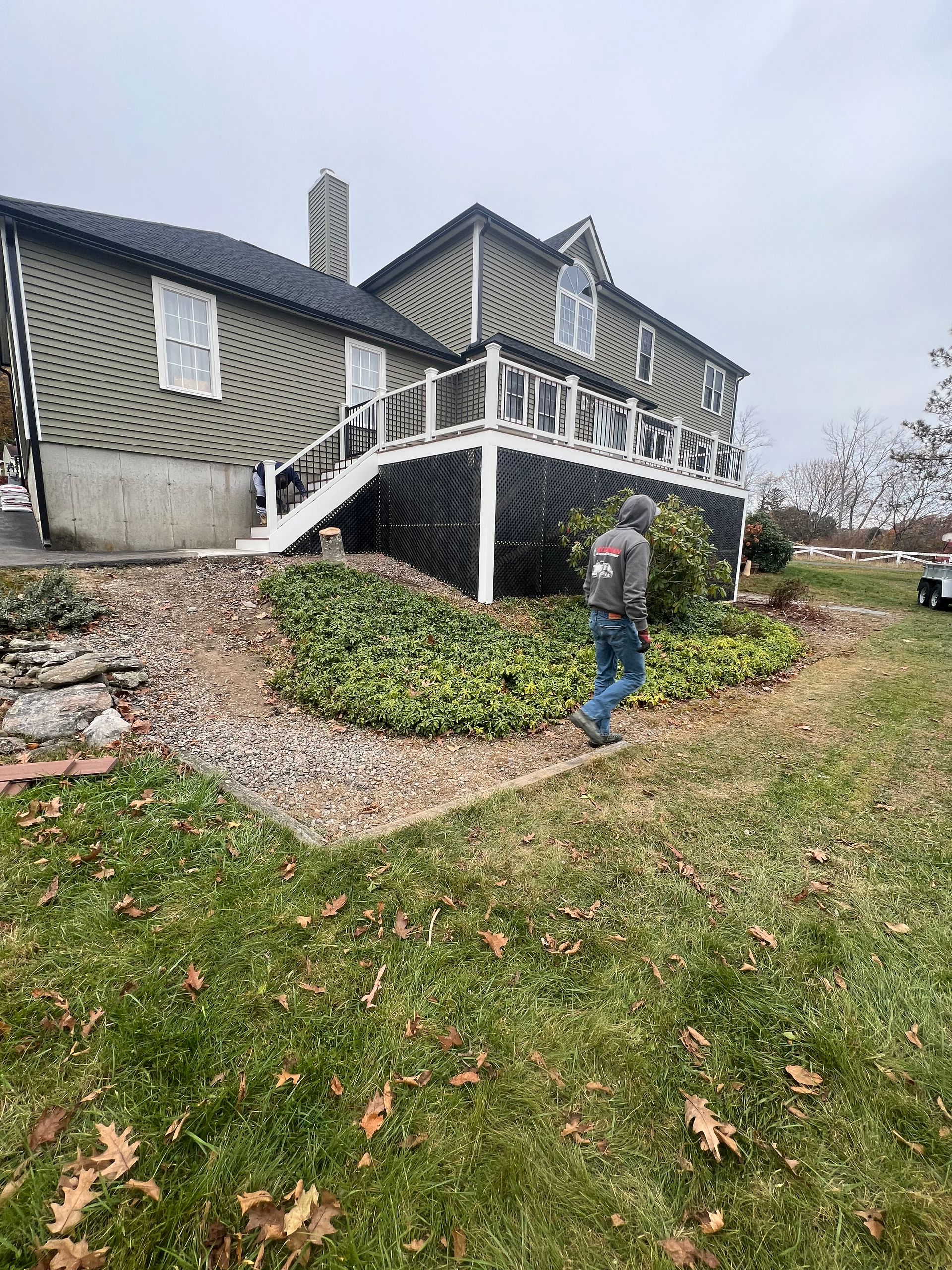 A man is walking in front of a large house with a deck.