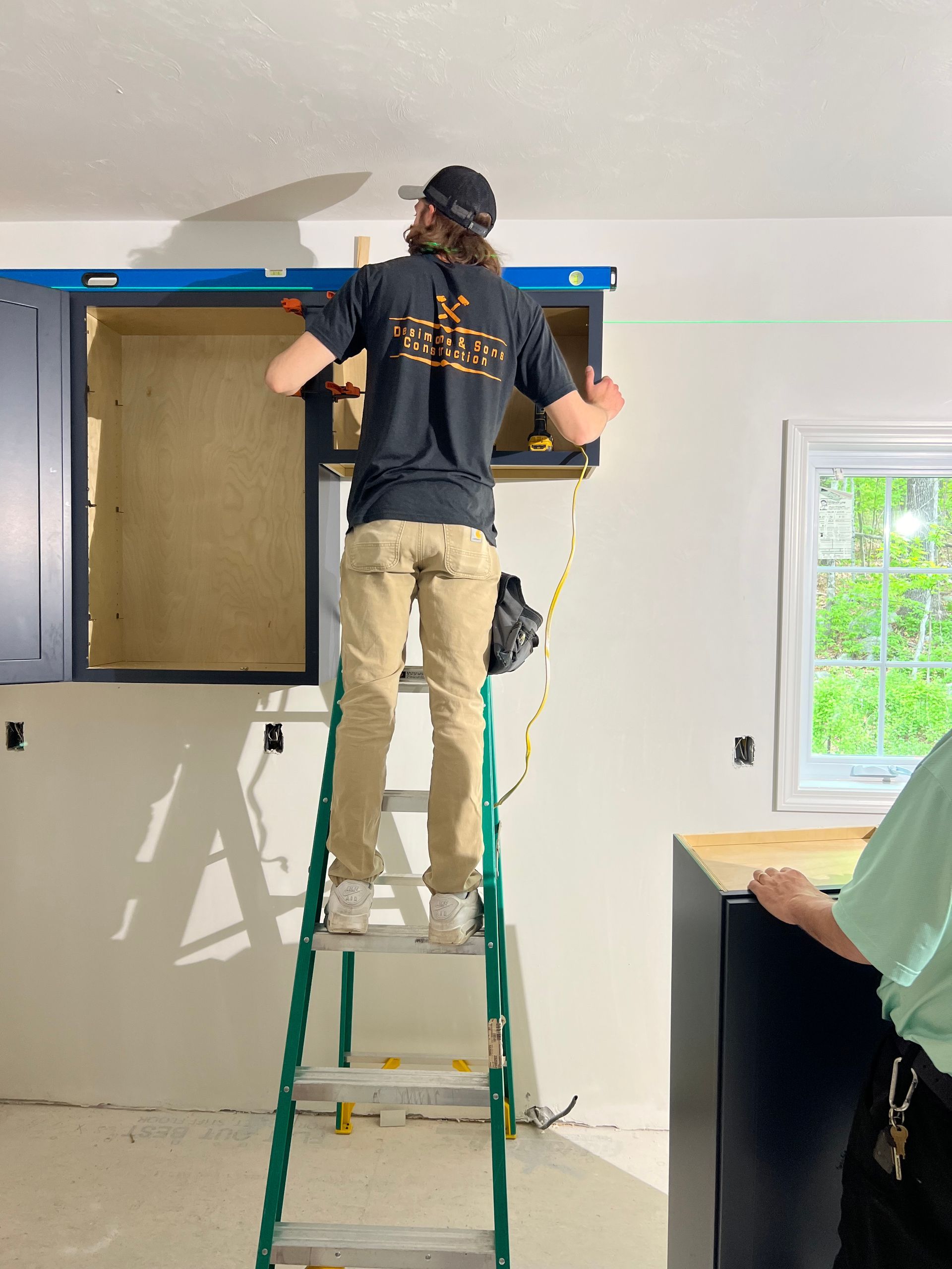 A man is standing on a ladder working on a kitchen cabinet.