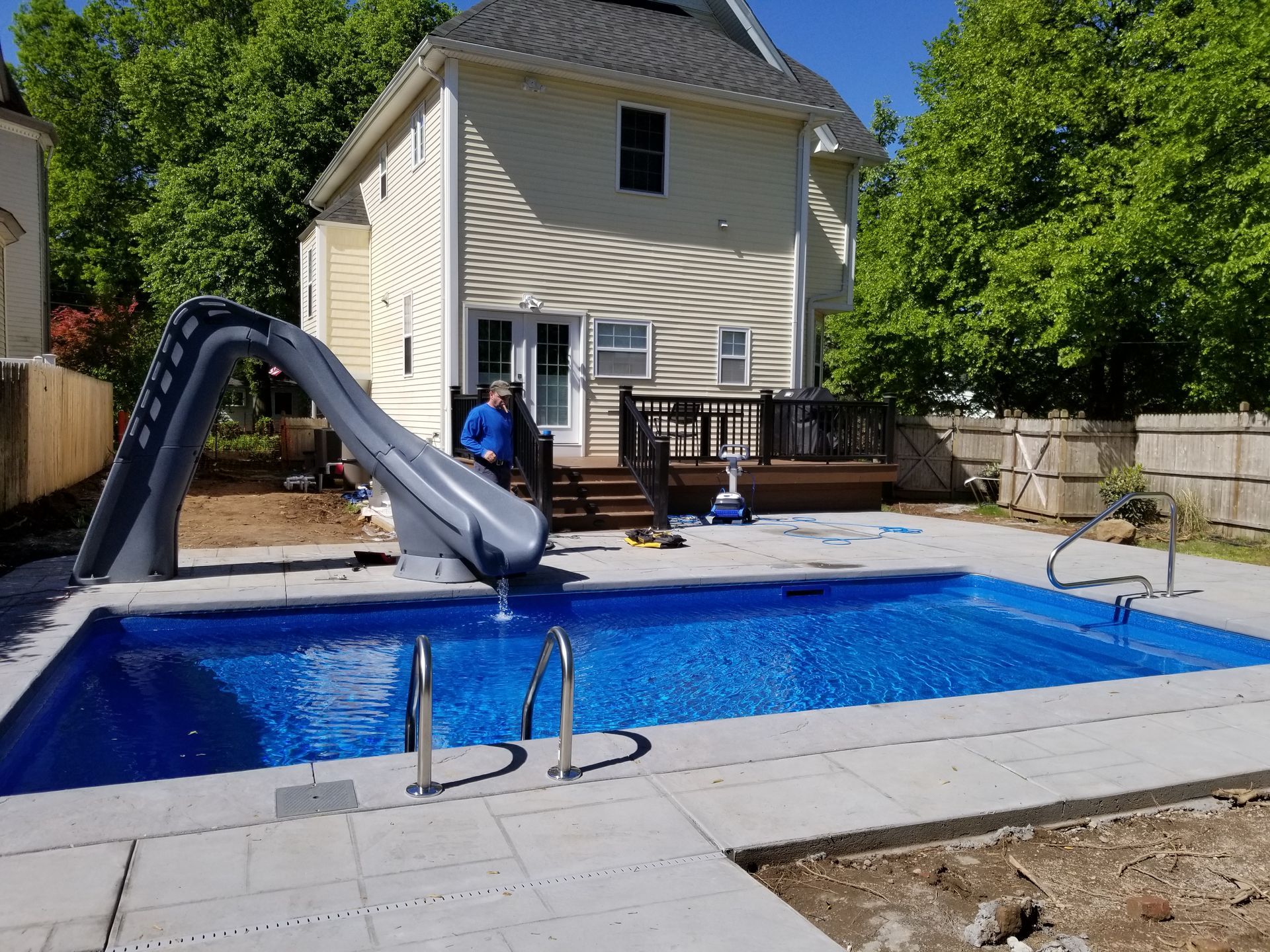 A man is standing next to a swimming pool with a slide attached to it.