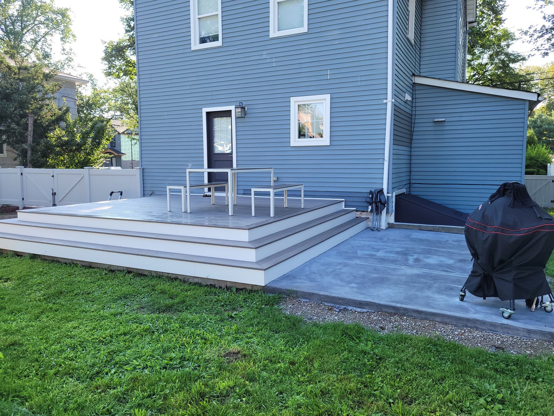 A blue house with a patio and a grill in front of it.