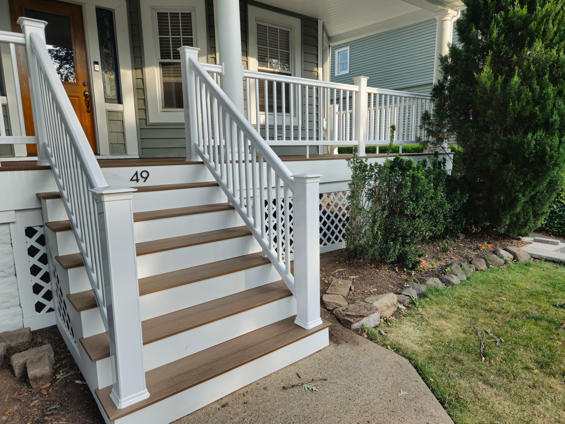 The front porch of a house has a white railing and stairs