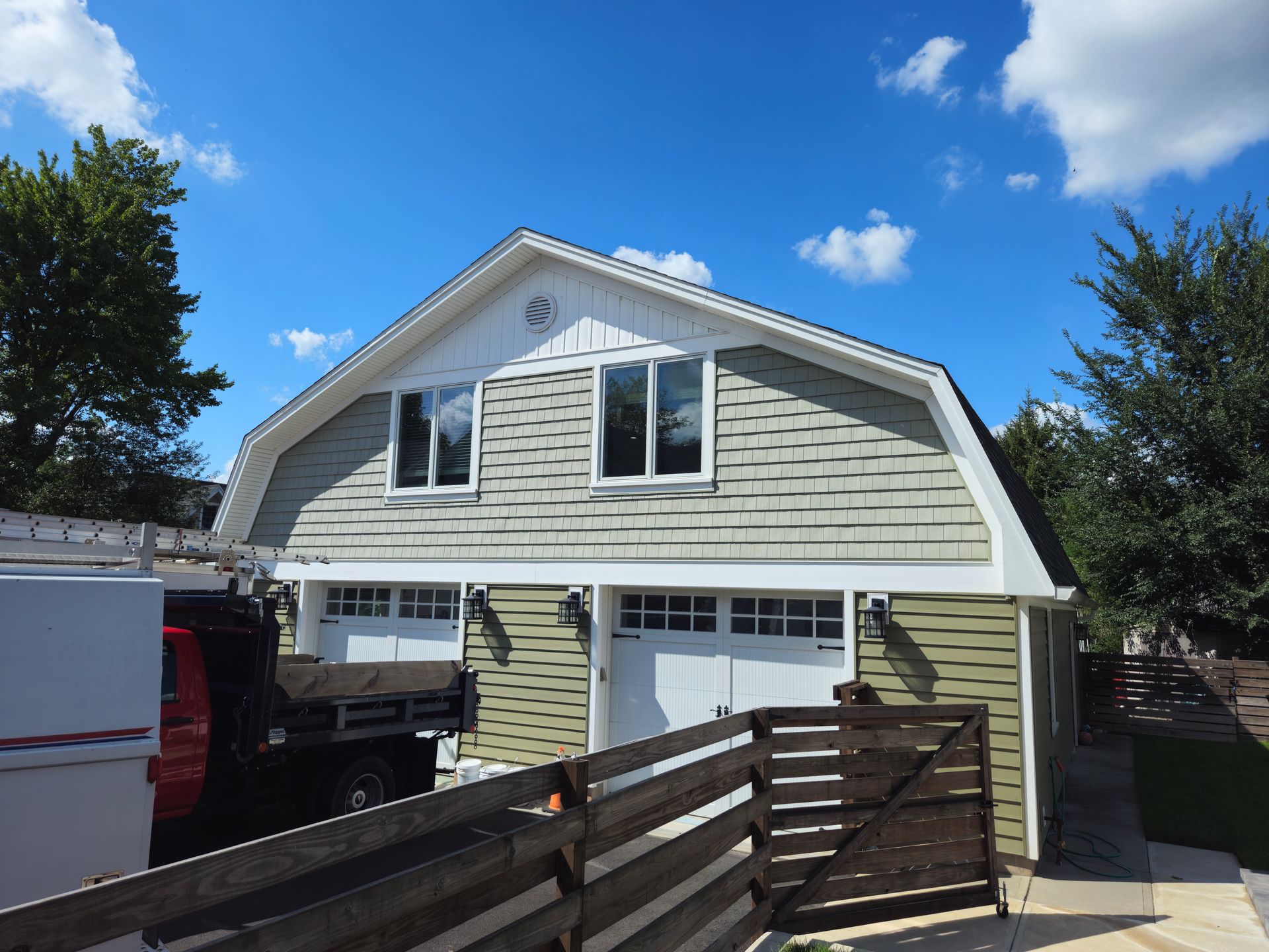A garage with a white roof and green siding is sitting next to a wooden fence.