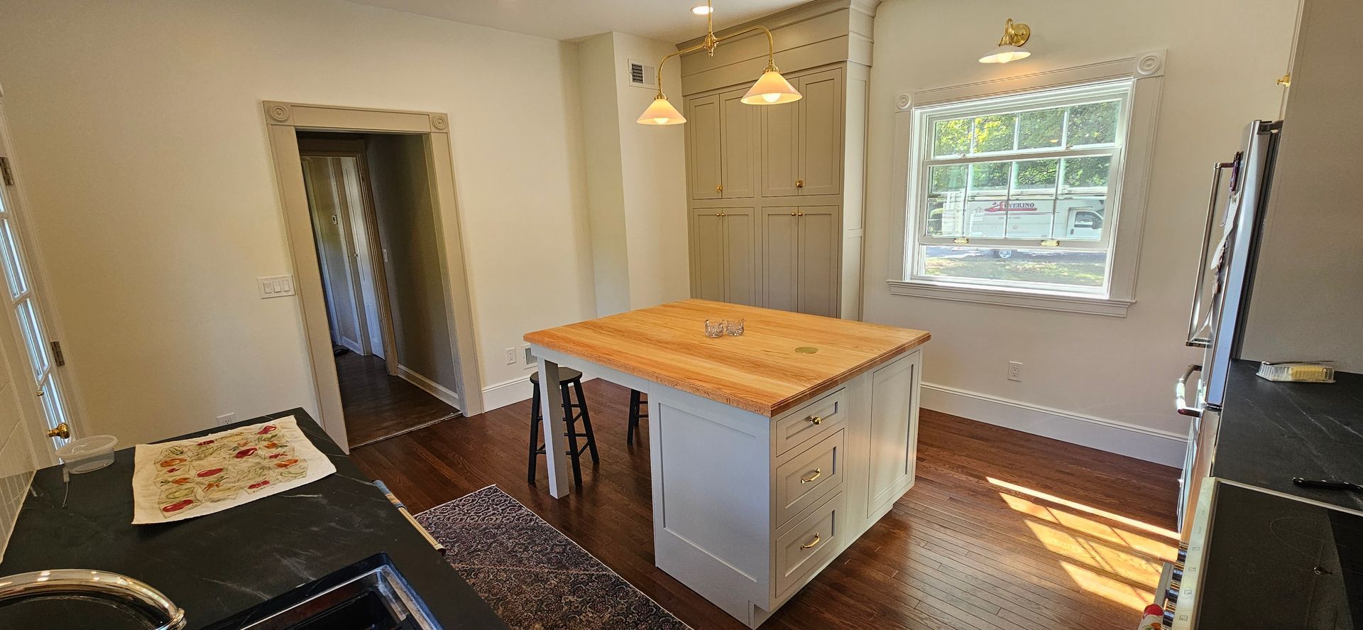 Kitchen with island, wooden floors, white cabinets, and wooden doors. Natural light streams from window.