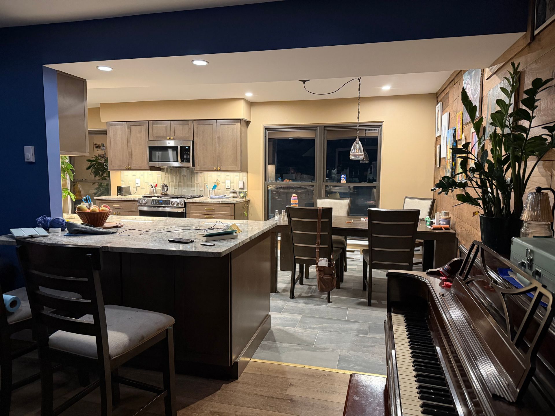 Kitchen with island, dining table, and piano. Brown cabinetry, beige walls, and dark flooring.