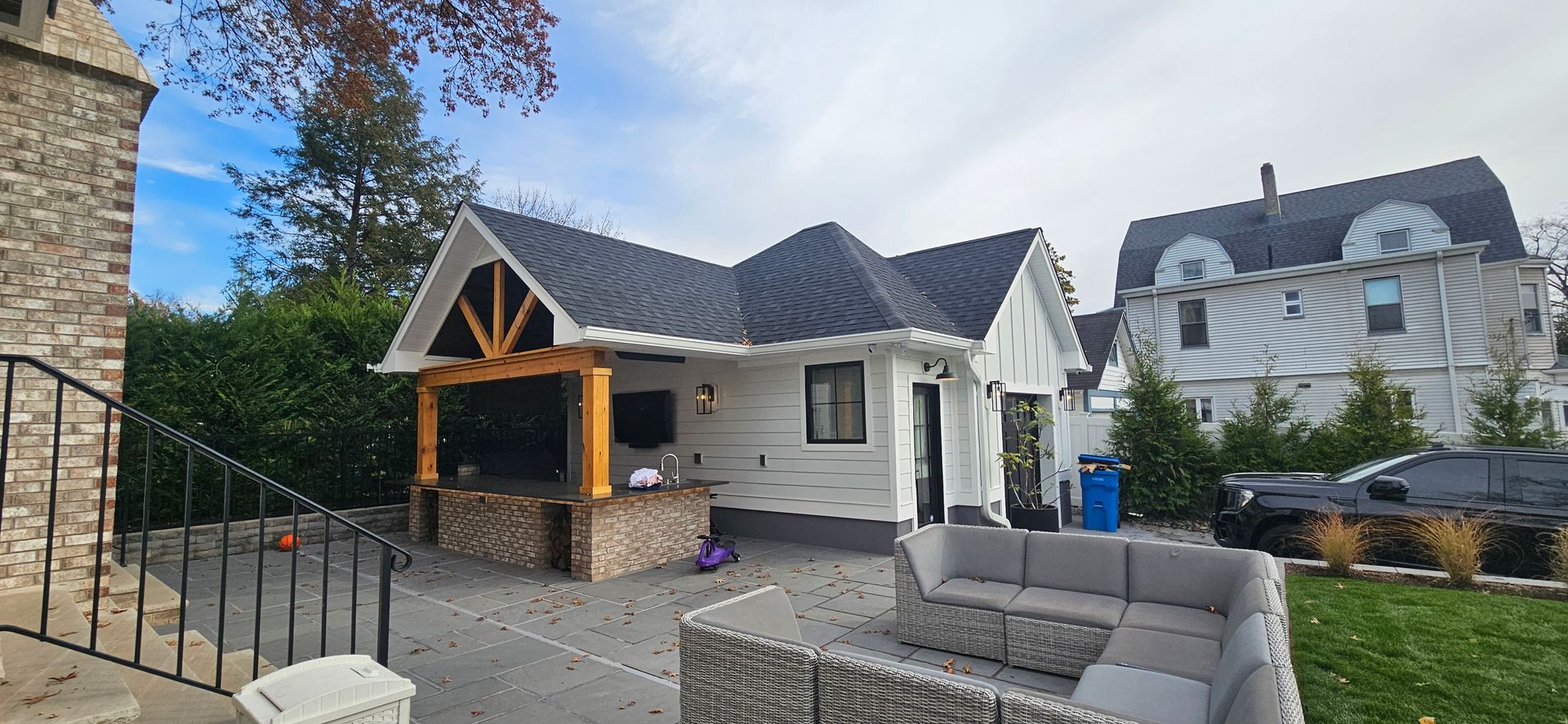 A white house with a black roof and a patio with gray furniture.