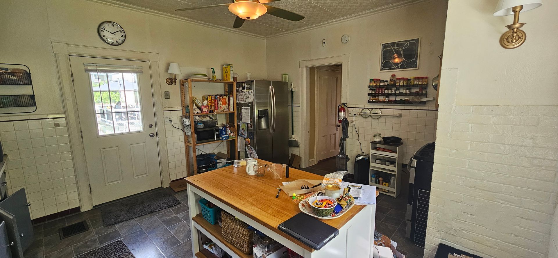Kitchen interior with island, stainless steel refrigerator, and open doorway.