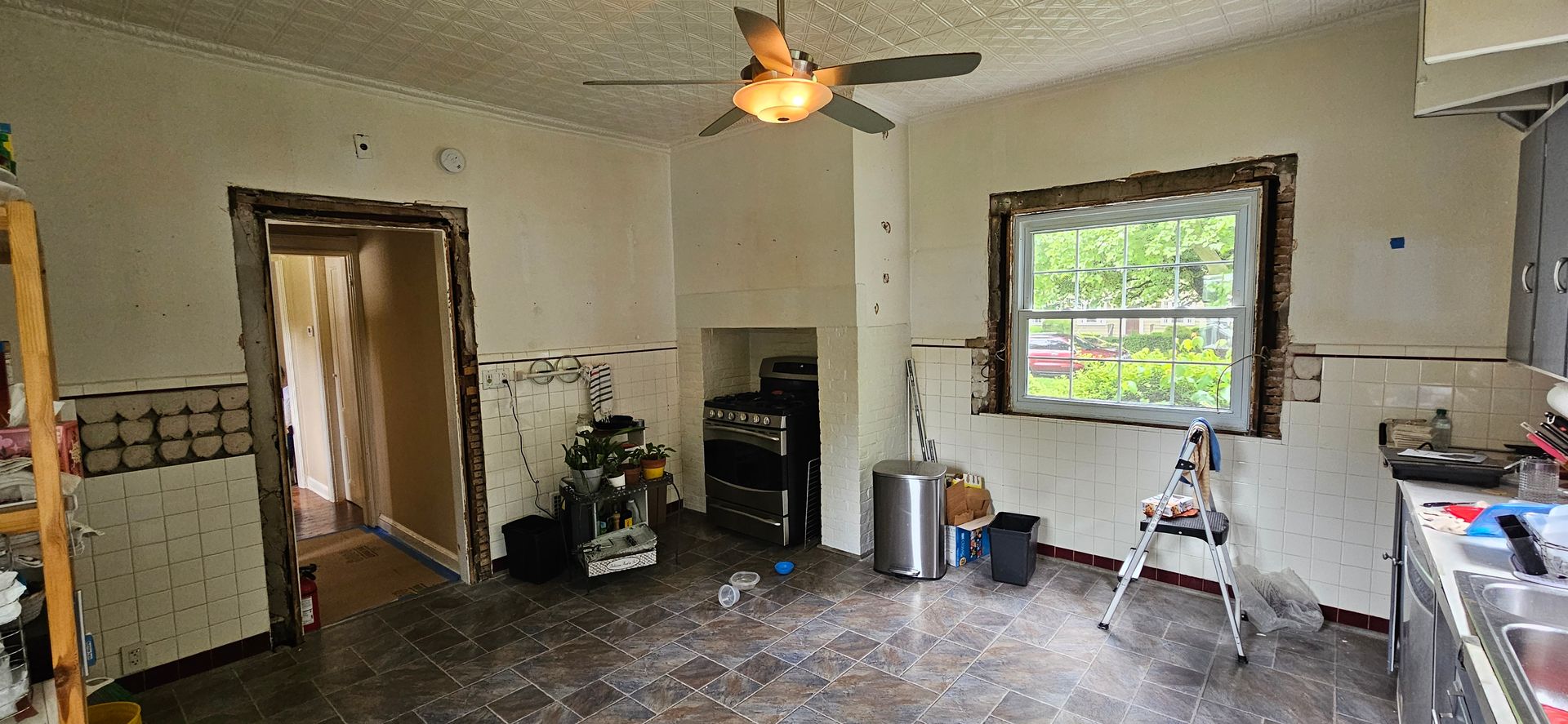 Interior of a room undergoing renovation, with visible ceiling fan, window, and debris on the floor.