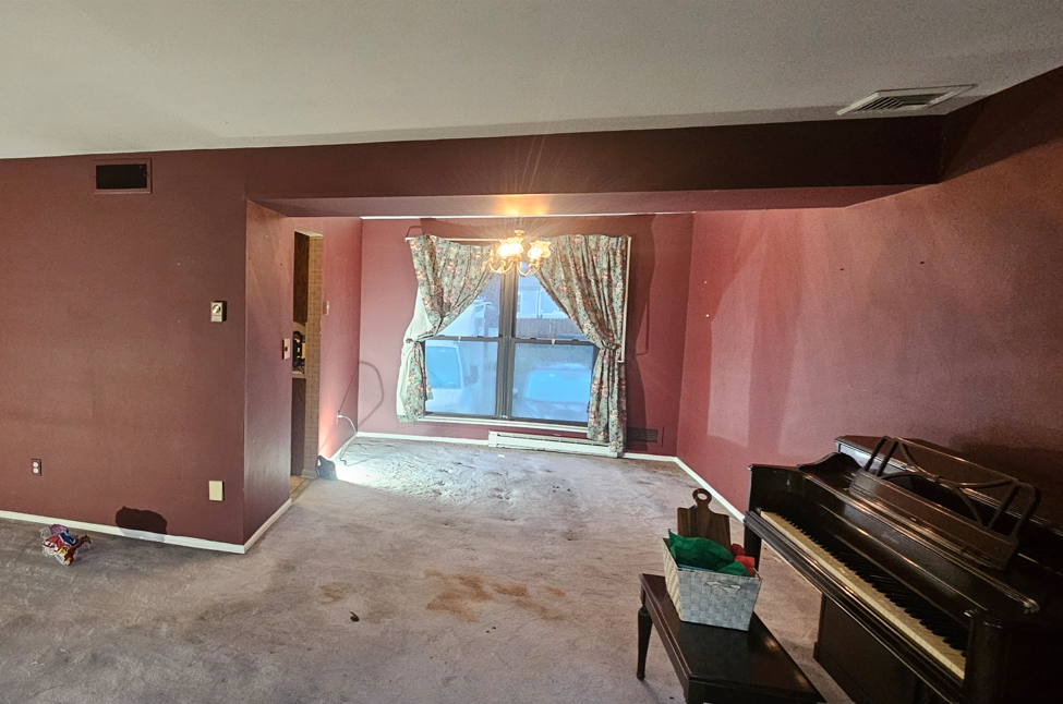 Room with burgundy walls, a window with curtains, a piano, and dirty carpet.