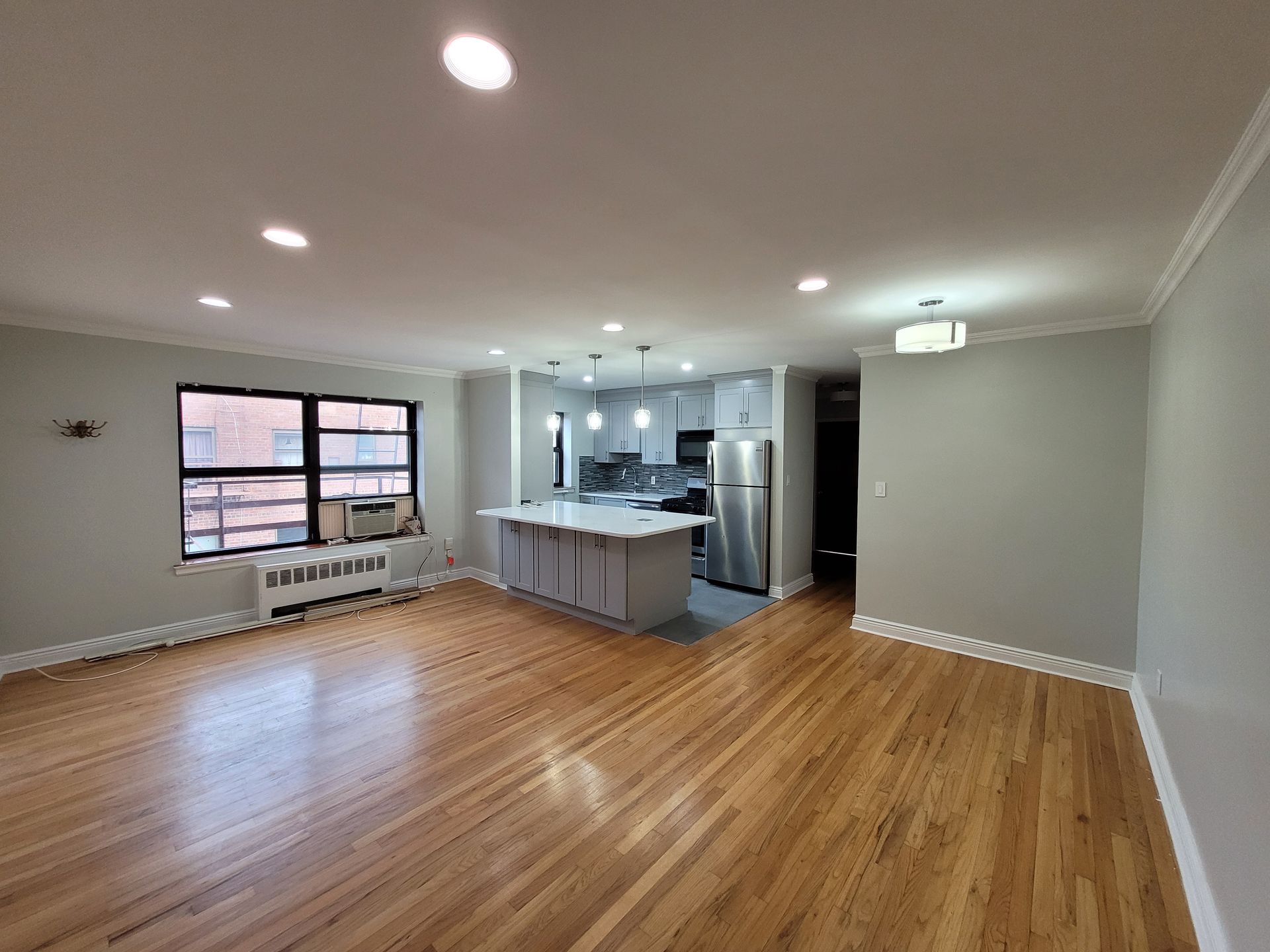 A living room with hardwood floors and a kitchen in the background.