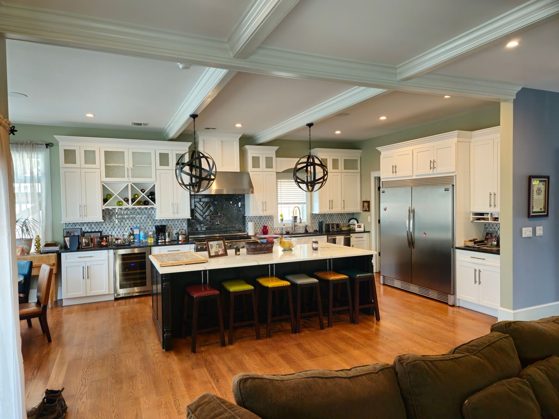 A kitchen with a large island and stools in a living room.