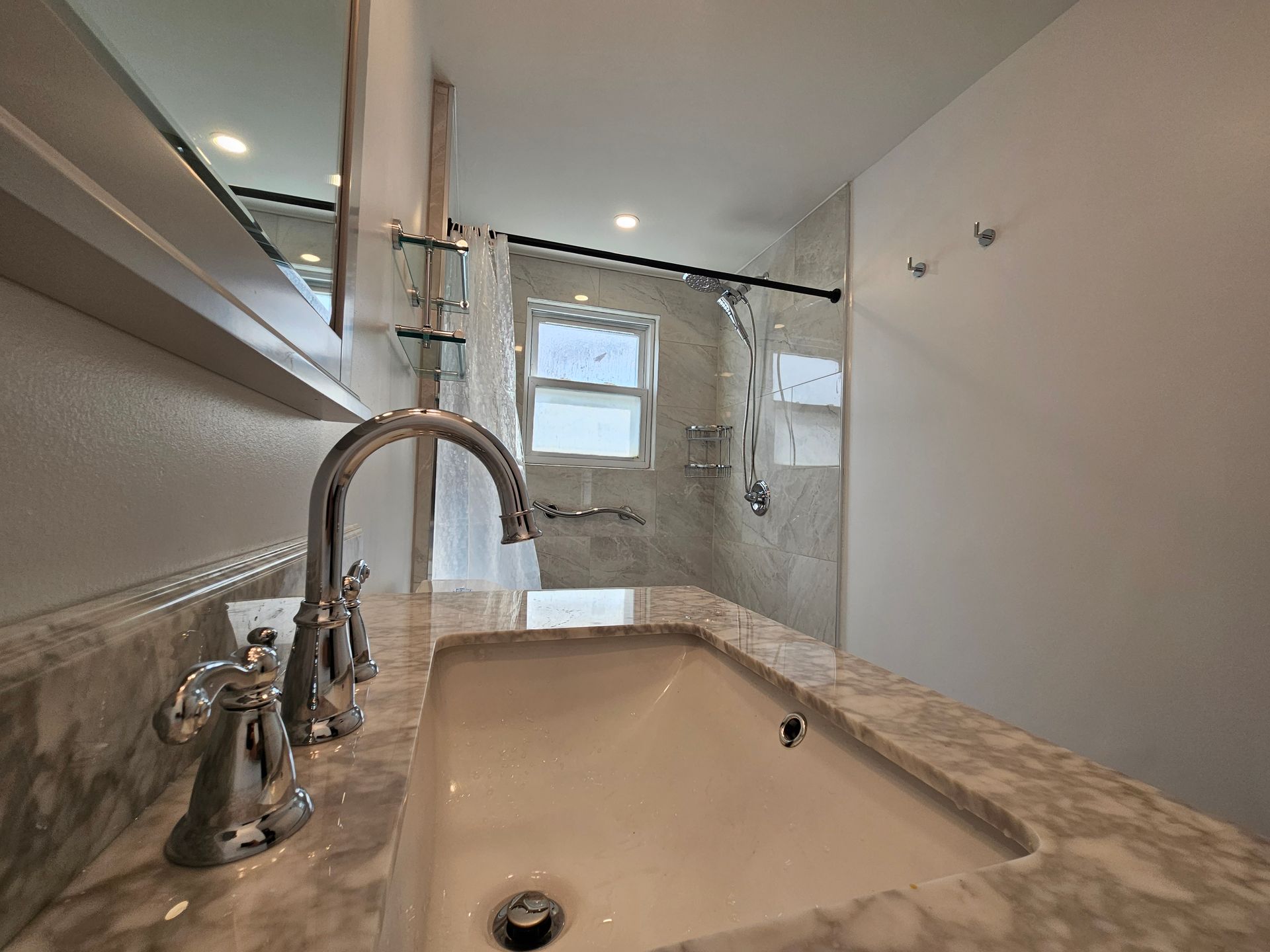 A bathroom with a sink, mirror and shower.