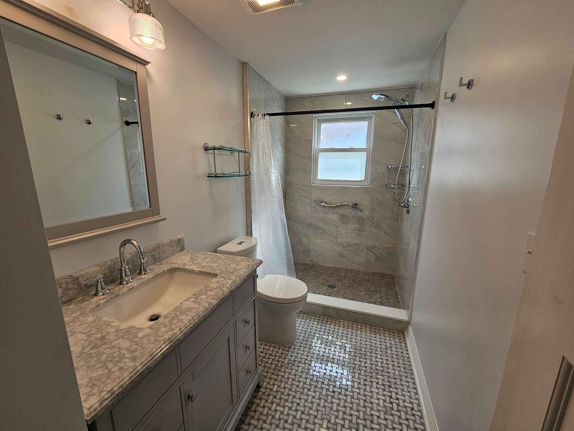 A bathroom with a sink, toilet, shower and mirror.