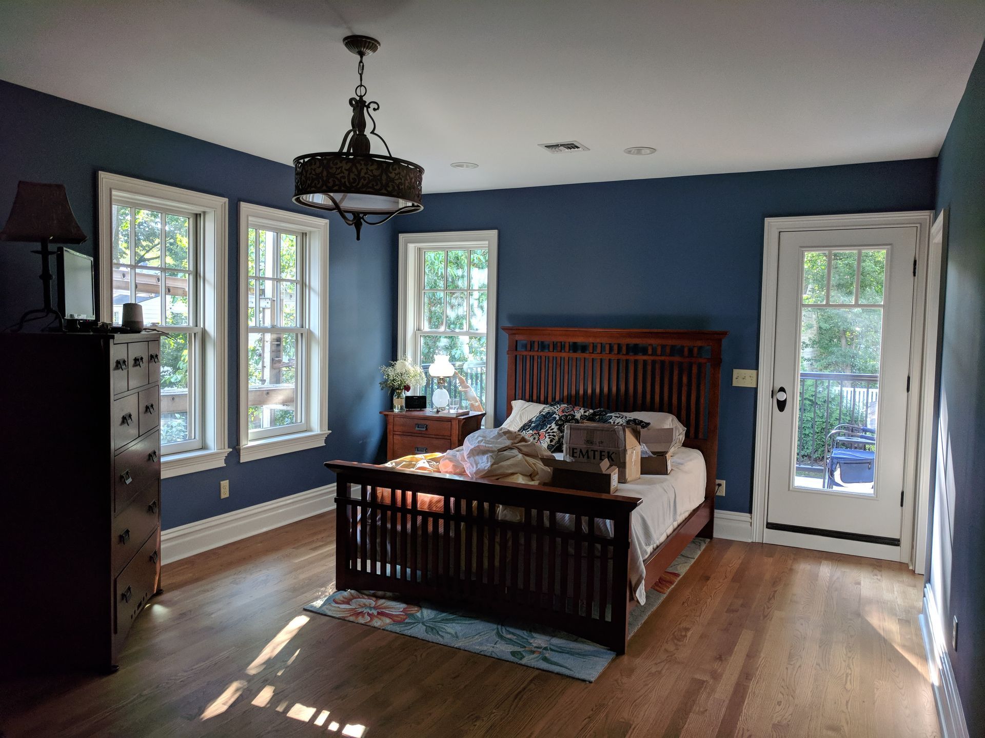 A bedroom with blue walls, a bed, a dresser, and a chandelier.