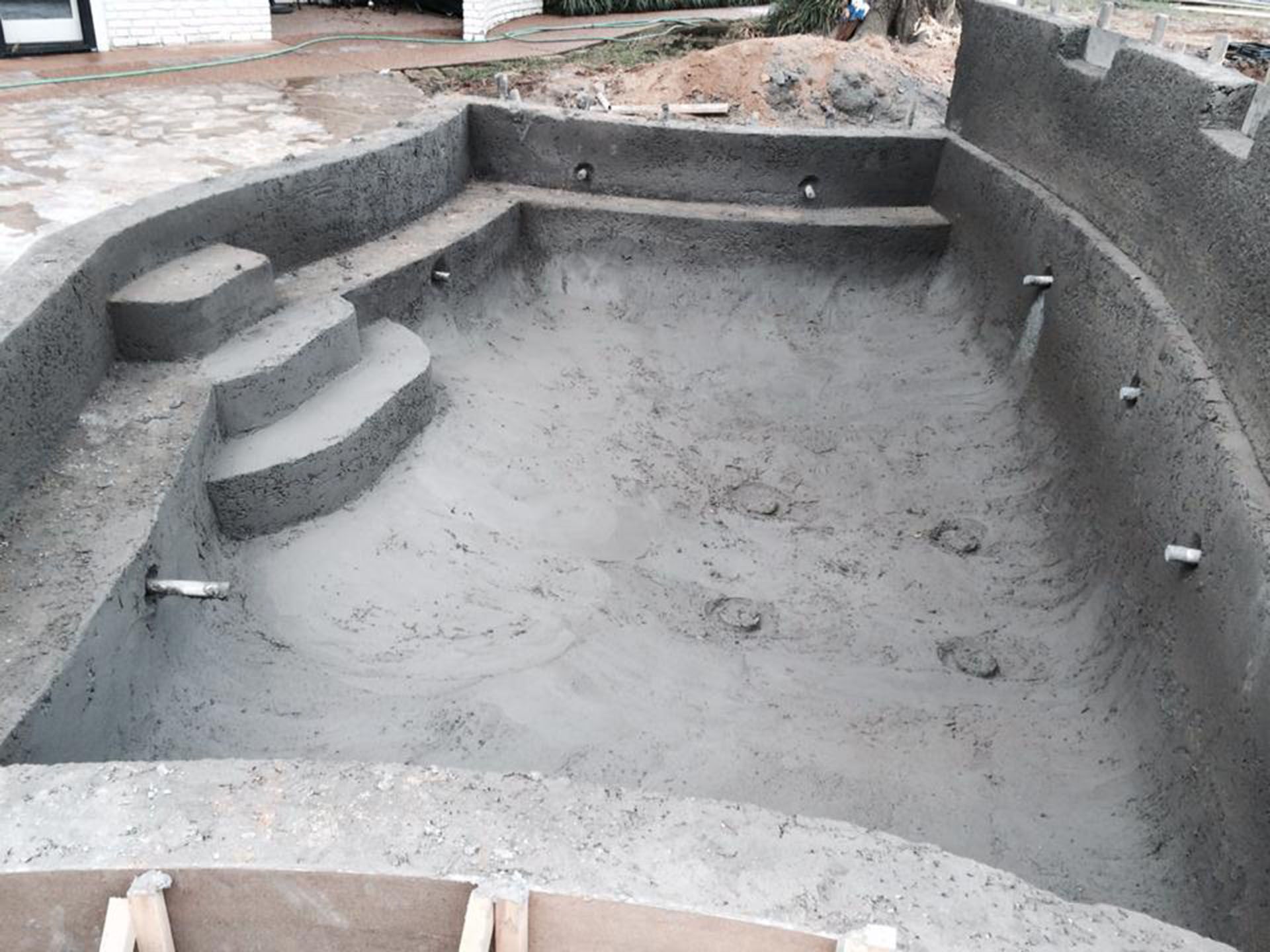 Concrete swimming pool under construction; steps, lights, and plumbing visible.