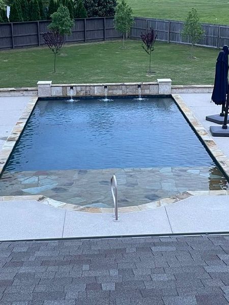 Rectangular swimming pool with water fountains, surrounded by stone and patio.