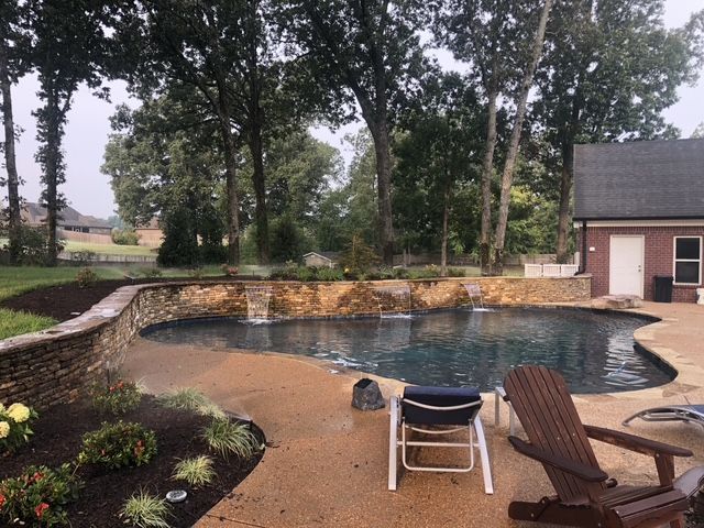 Swimming pool with stone waterfall, surrounded by landscaping, patio, trees, and house.