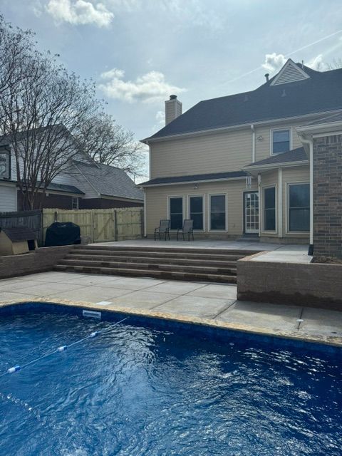 Backyard with pool, concrete patio, steps leading to the house, and a fence. The house is tan.
