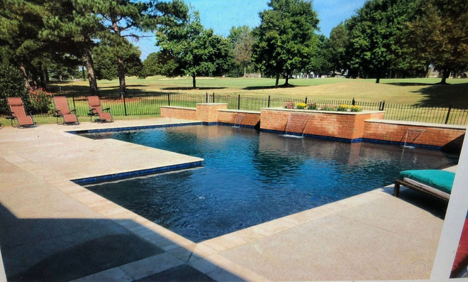 Pool with dark blue water and stone surround, patio with lounge chairs. Trees and grass in background.