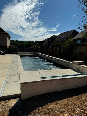 Rectangular pool with concrete surround in a backyard on a sunny day.