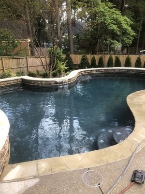 Pool with dark blue water and stone edging, surrounded by a paved patio and a wooden fence.