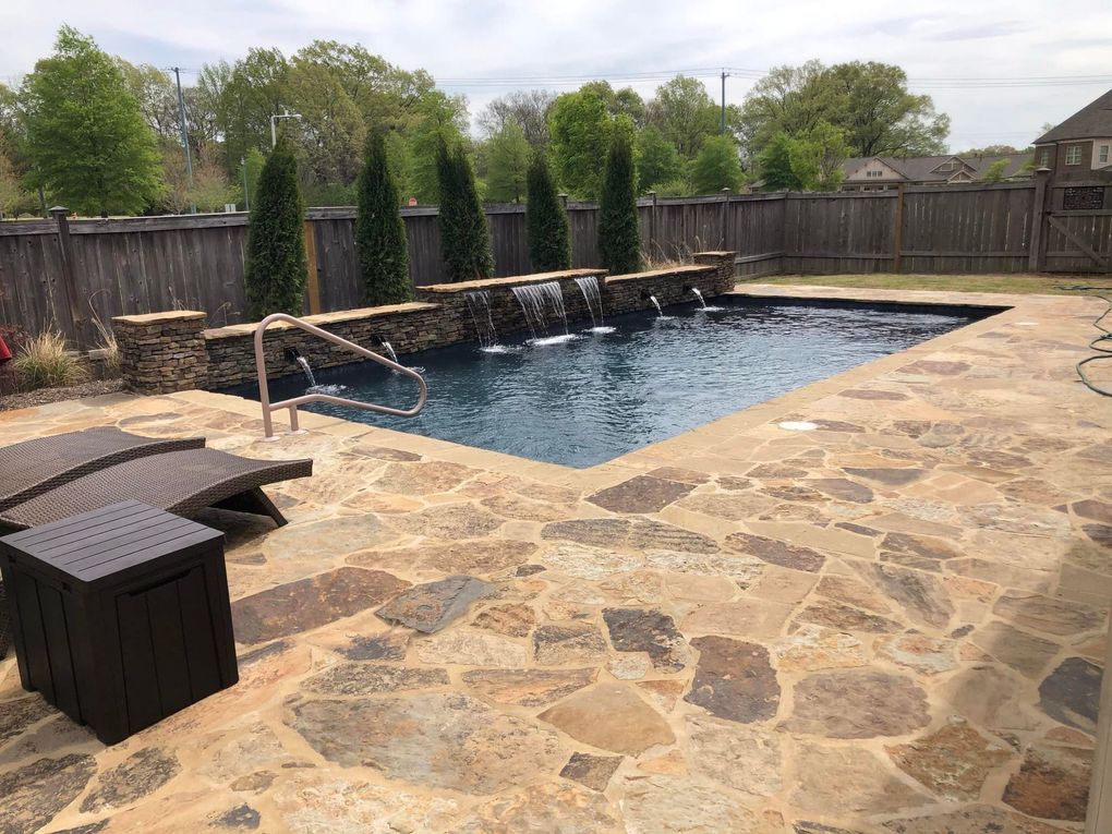 Backyard swimming pool with stone patio, water feature, and dark blue water.