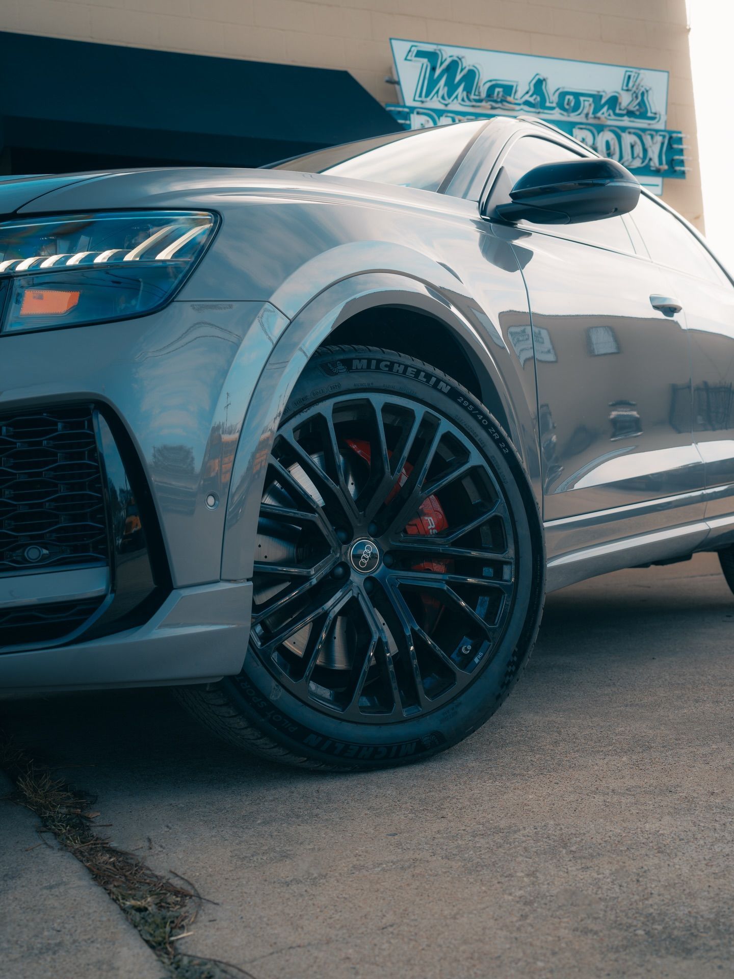 Gray SUV with black wheels parked in front of a body shop, showcasing its front side.