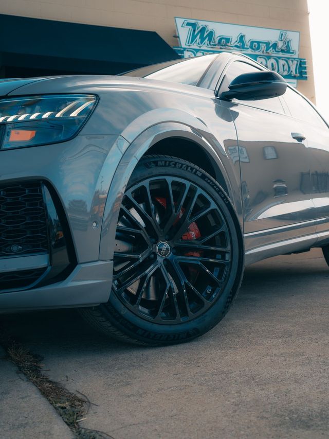 Gray SUV with black wheels parked in front of a body shop, showcasing its front side.