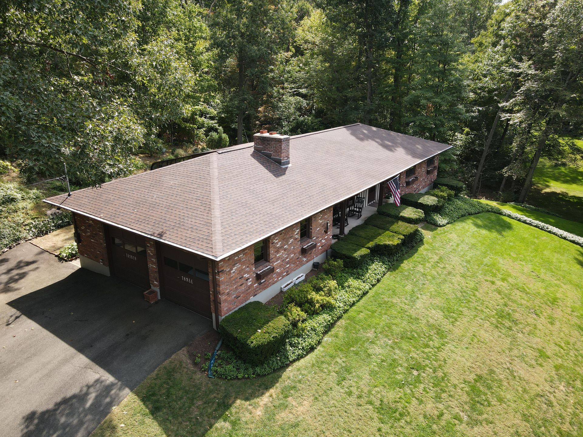 An aerial view of a brick house with a large lawn and trees in the background.