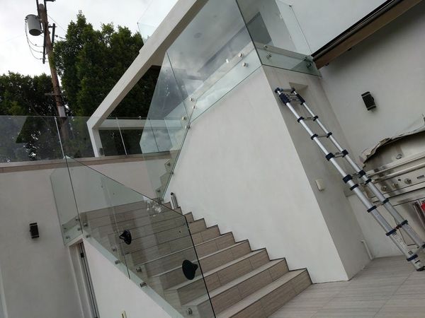 Modern outdoor staircase with glass railings beside a white building and tall ladder.