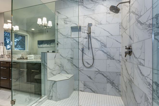 Modern marble-tiled bathroom with glass shower, rainfall showerhead, and vanity visible through the doorway
