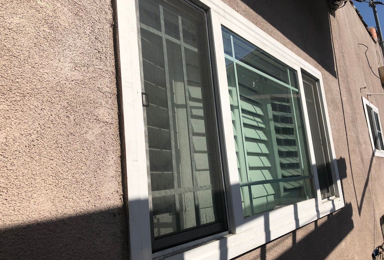 Sunlit building exterior with a large window, white trim, and beige stucco wall