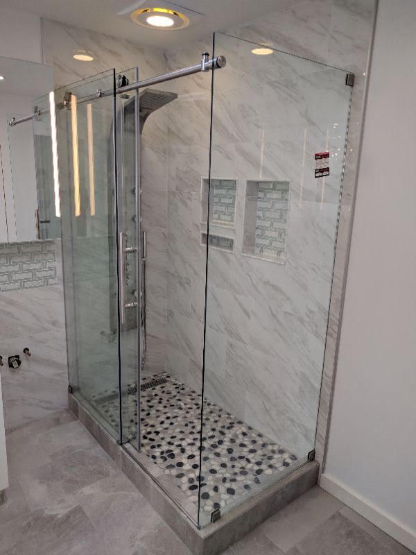 Glass shower enclosure with marble walls and black-and-white tile floor in a bathroom.