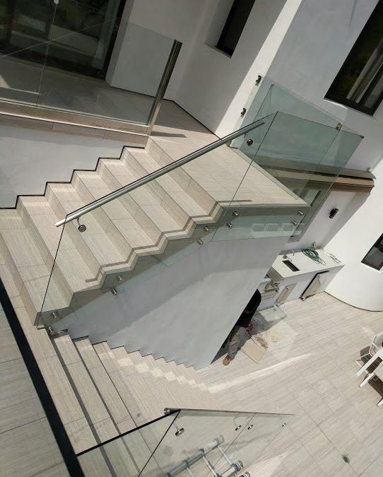Modern indoor staircase with glass railings and white tiled steps in a bright, open interior