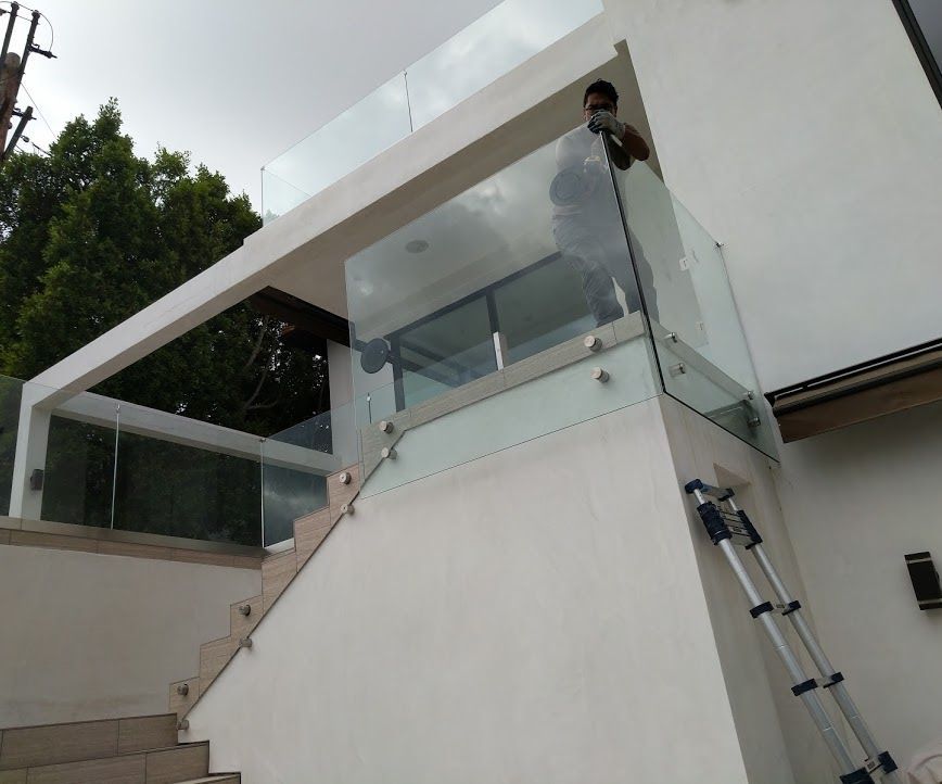 Modern outdoor stairway with glass railings and a ladder leaning against a white wall.
