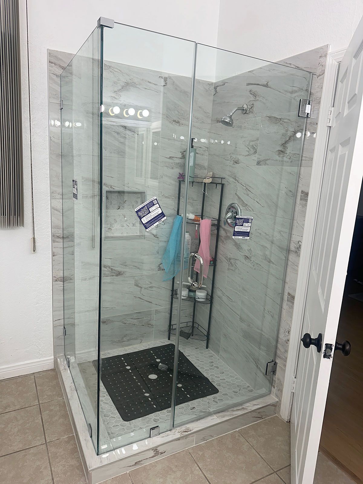 Glass walk-in shower with marble walls, black floor mat, and hanging towels