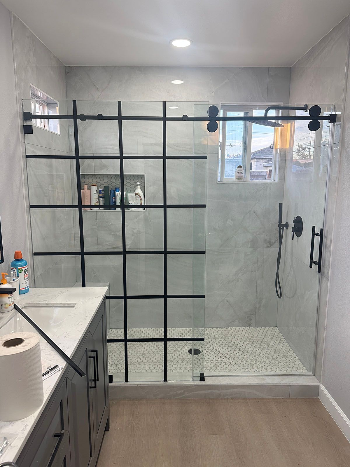 Modern bathroom with glass shower enclosure, gray tiled walls, and vanity countertop