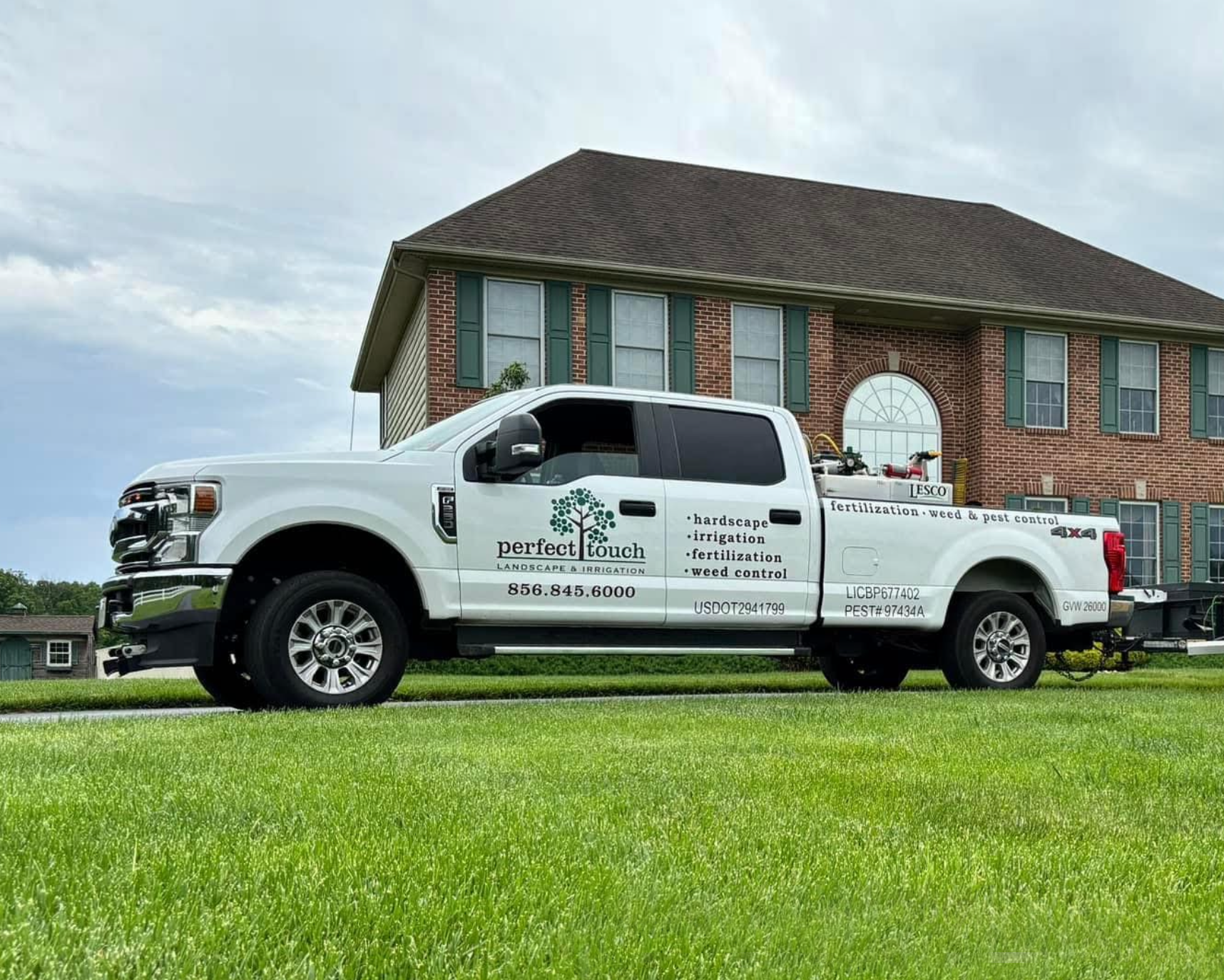 A white truck is parked in front of a brick house.