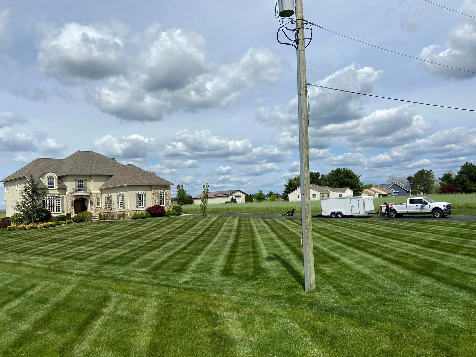 A large lawn with a house in the background and a trailer parked in front of it.