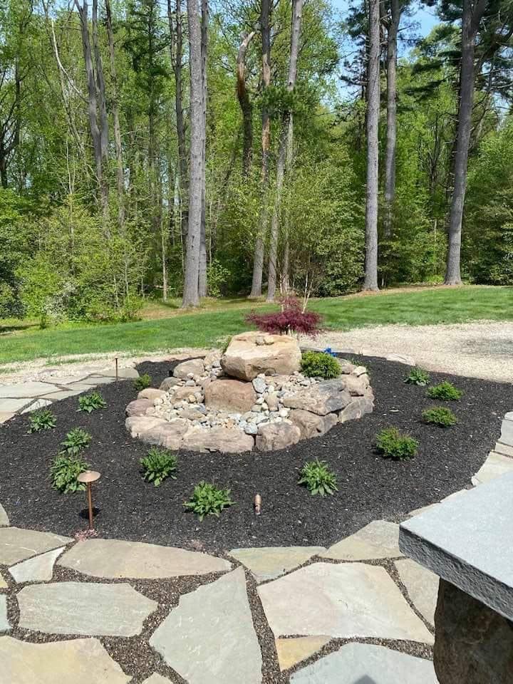 A stone patio with a fountain in the middle of it surrounded by trees.