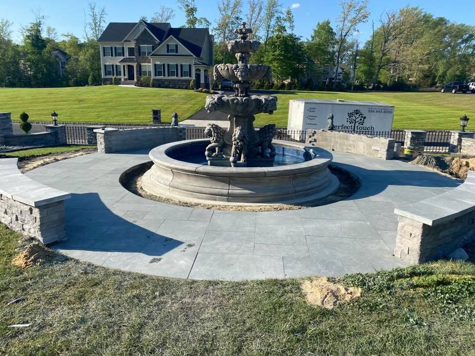 A large fountain is in the middle of a lush green field in front of a large house.