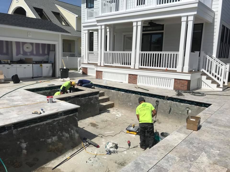 Two men are working on a swimming pool in front of a house.