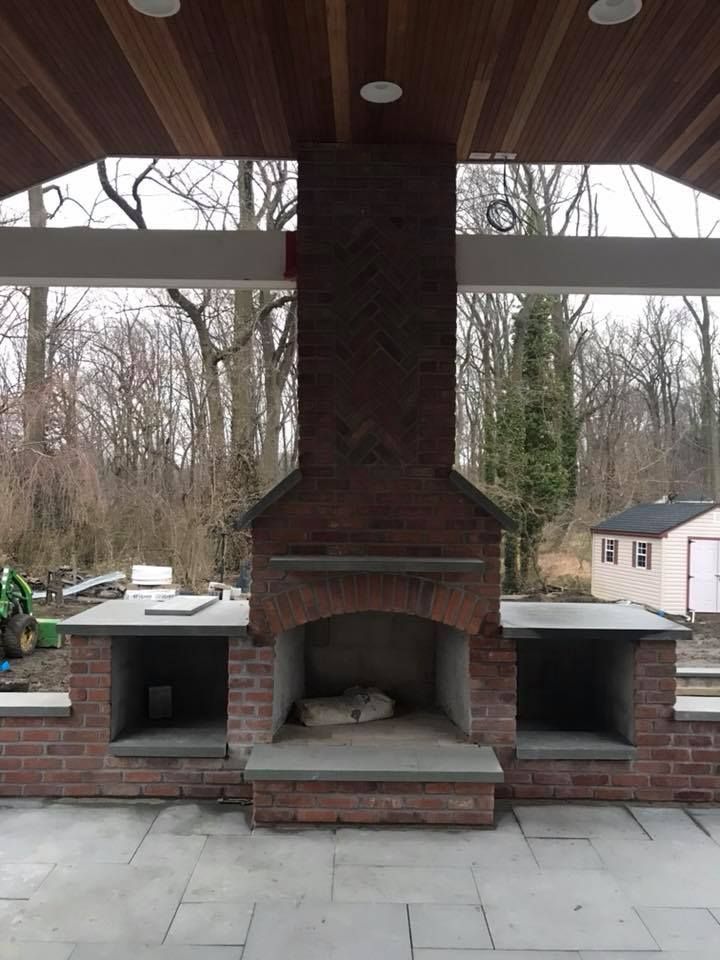 A brick fireplace under a covered area with trees in the background