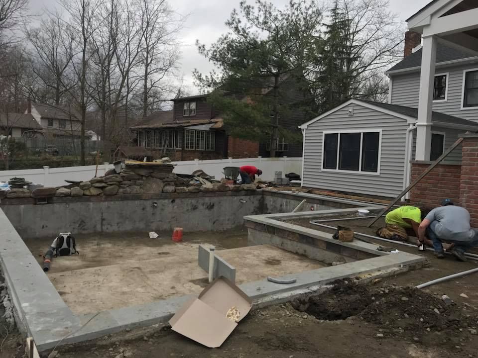 A group of men are working on a swimming pool in front of a house.