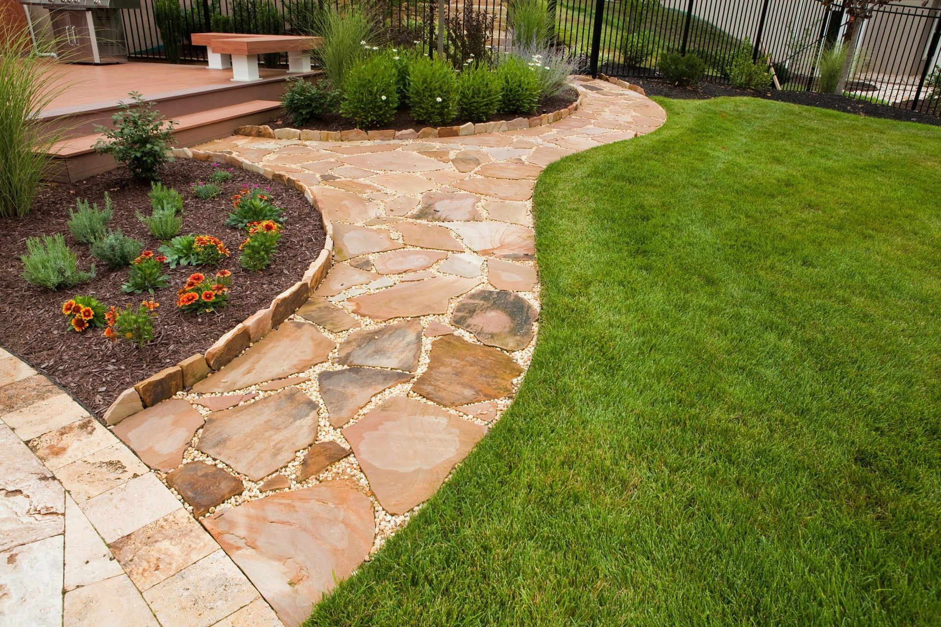 A stone walkway in a backyard surrounded by grass and flowers.